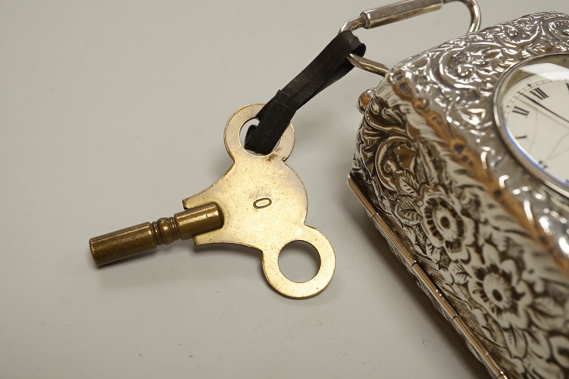An early 20th century white metal (tests as silver) carriage timepiece, with white Roman dial (cracks) and case embossed with foliage, on four ball feet, 76mm excluding handle, with key.